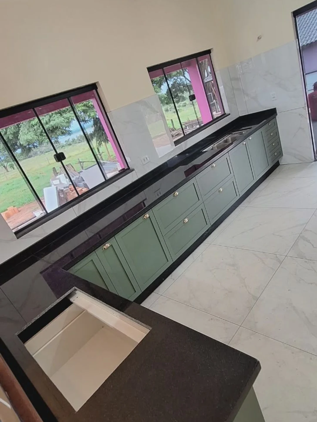 Bancada longa de granito preto em cozinha com armários verdes